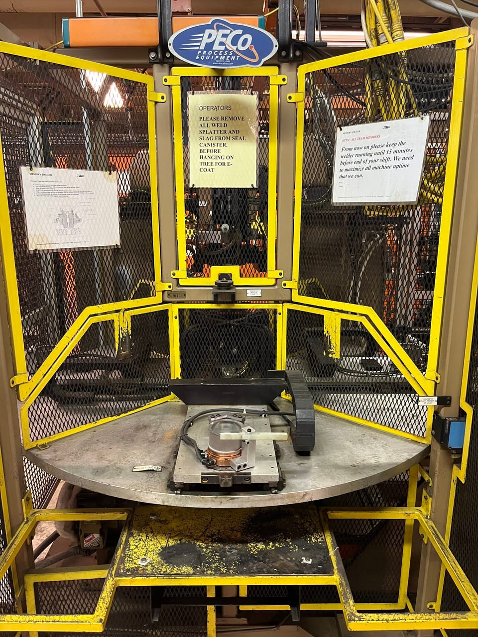 A PECo welding machine and workpiece inside a yellow safety enclosure