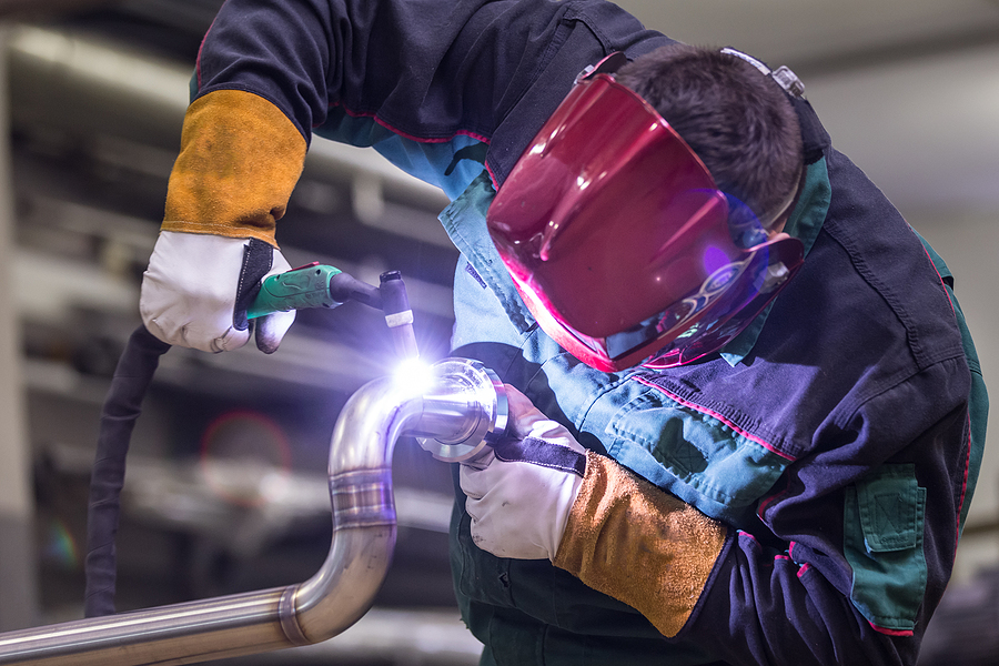 Industrial worker with protective mask welding inox elements in steel structures manufacture workshop.